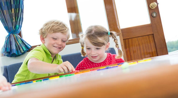 2 Kinder spielen an einem Holztisch auf einem Hausboot aus der Kuhnle Werft